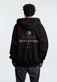 Sort hættetrøje med stort rygprint i lysegrå. Har et logo, tekst og en kengurulomme. Stoffet ser blødt og afslappet ud.