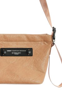 Bolso bandolera de cuero sintético color marrón claro con acabado texturizado, un parche negro con la marca y una correa desmontable con herrajes plateados.