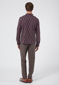 Camisa de manga larga en morado oscuro con un patrón de diamantes, con un corte relajado y puños con botones, combinada con pantalones beige texturizados y zapatillas multicolores.