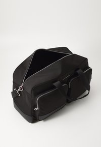 Sac de sport noir avec une surface texturée, fermetures à glissière argentées, deux poches avant et des poignées de transport doubles. Conception à ouverture supérieure.