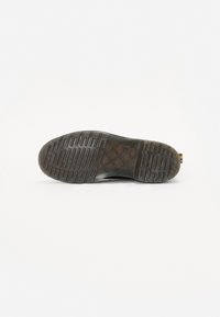 Zwarte rubberen zool met getextureerd profiel, met horizontale en verticale groeven voor grip, ronde teen en een hielband voor gemakkelijk aan- en uittrekken.