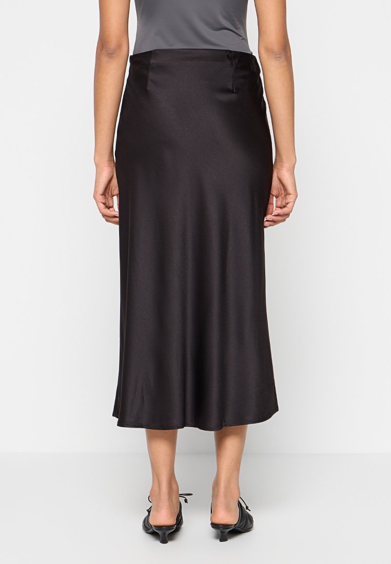 Schwarzer Satin-Midirock mit glatter Textur, ausgestelltem Saum und einem verdeckten Reißverschluss auf der Rückseite, kombiniert mit schwarzen spitzen Schuhen.