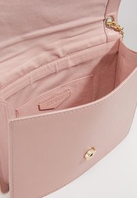 Borsa in pelle rosa chiaro aperta per mostrare l'interno in tessuto con una piccola tasca etichettata "TOPSHOP" e un attacco in catena dorata.