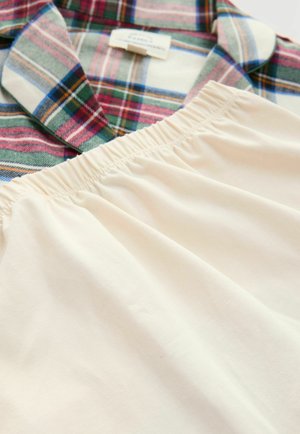 Geruite shirt in groen, rood, blauw en wit naast een beige stof met elastische tailleband, plat liggen op een witte ondergrond.