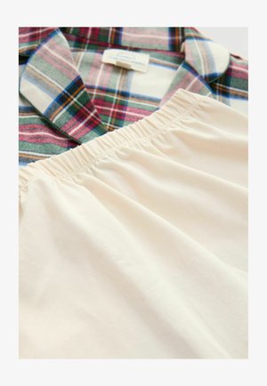 Rutet skjorte i grøn, rød, blå og hvid ved siden af beige stof med elastisk talje, lagt fladt på en hvid overflade.