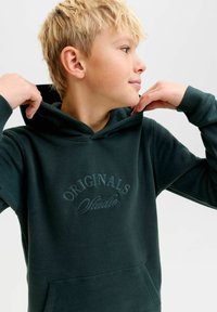 Sudadera con capucha de color verde oscuro con cordón, que presenta un logo bordado "ORIGINALS Studio" en el pecho y puños acanalados. Textura suave.