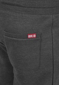 Graue Jogginghose mit geripptem Bund, seitlicher Tasche und einem roten "!SOLID"-Logo-Tag. Das Material ist weich und strukturiert.