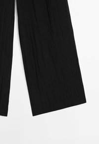Pantalon noir à jambes larges en tissu texturé à l'aspect froissé, présentant une coupe ample et des bords d'ourlet nets.