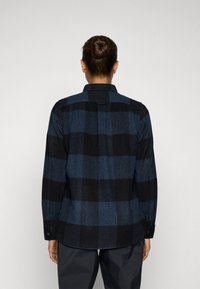 Zwart en blauw geruite flanellen overhemd met knoopmanchetten en een schouderstuk aan de achterkant, met een licht gebogen zoom en textielstructuur.