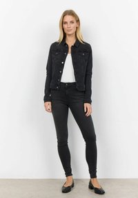 Svart denimjacka med två bröstfickor, silverknappar och tighta svarta jeans. Modellen bär en vit topp och svarta ballerinas. Slät textur.
