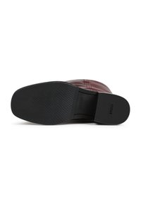 Bota vermelha em couro com uma sola de borracha preta texturizada e parte superior lisa, apresentando um design subtil e o logótipo em relevo na sola.