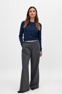 Navy gebreide cardigan met knoopsluiting, gecombineerd met hooggetailleerde, wijde grijze broek met een subtiele streep.