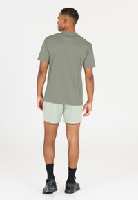 Oliivinvihreä lyhythihainen paita, vaaleanvihreät shortsit, mustat urheilukengät ja mustat sukat. Silkkinen kangas rentoa istuvuutta.