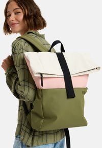 Ryggsäck med vikbar topp i vitt och rosa, en olivgrön kropp och svarta remmar. Materialet verkar hållbart med en slät textur.