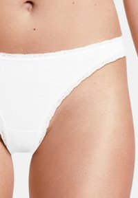 Perizoma bianco con pizzo, realizzato in un tessuto morbido ed elasticizzato. Presenta una vita liscia e un taglio classico con copertura minima.
