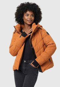 Jachetă puffer portocalie cu un design matlasat, cu fermoar în față, glugă ajustabilă și accente negre la manșete. Purtați peste un top negru și blugi.
