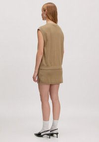 Beige ärmelloses Strickoberteil, das mit einem Rock kombiniert ist. Verfügt über gerippte Kanten, Seitenschlitze und wird mit grauen Socken und schwarzen Absatzschuhen gestylt.