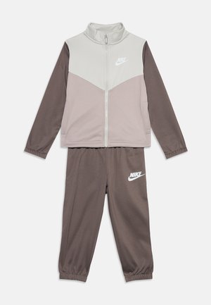 To-delt Nike joggingdragt til børn med lynlåstrøje i beige og brune toner og matchende brune bukser med Nike-logo på begge dele.