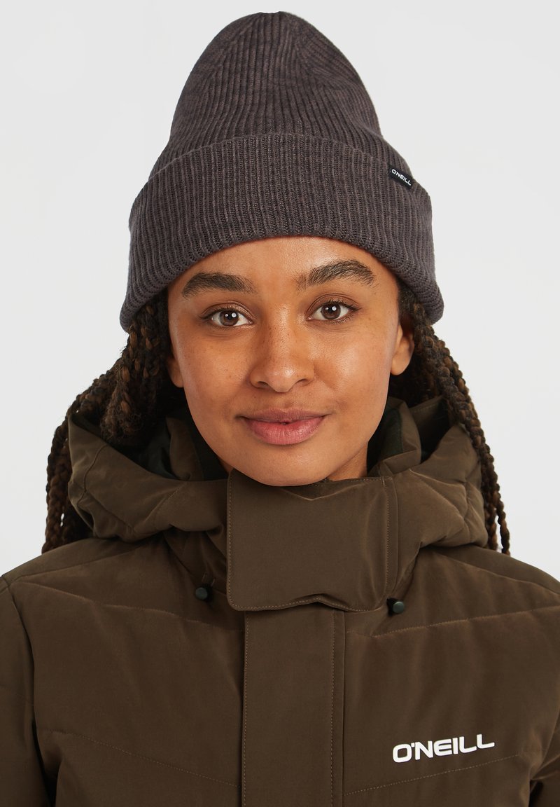 Giacca puffa marrone con colletto alto, abbinata a un berretto a coste grigio scuro. Presenta il logo O'Neill sulla giacca. Texture morbida, design casual.