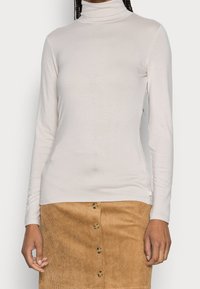 Vaaleanbeige poolopaita, jossa pitkät hihat ja pehmeä materiaali, yhdistetty ruskeaan ribbineulottuun samettihameeseen, jossa on napit detaljeina.