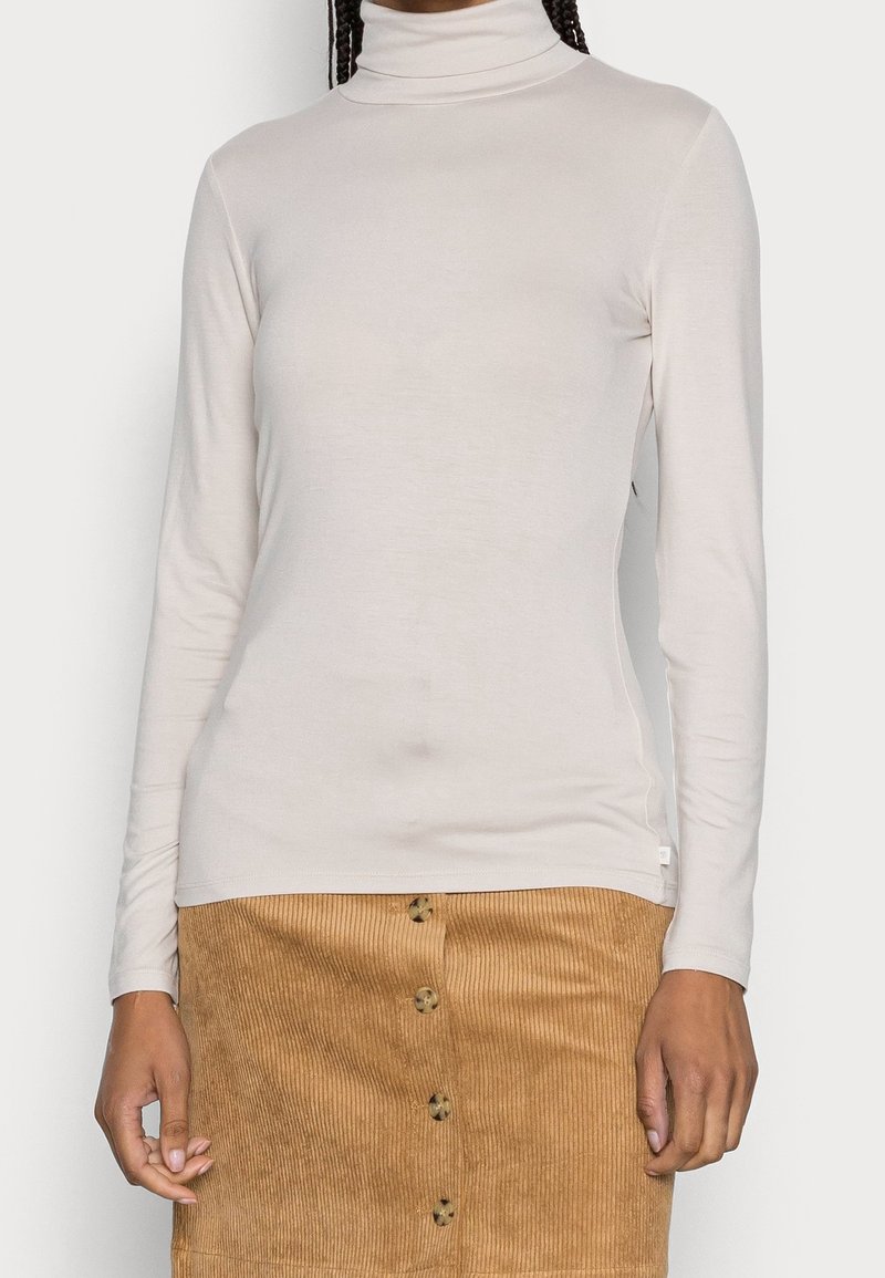 Vaaleanbeige poolopaita, jossa pitkät hihat ja pehmeä materiaali, yhdistetty ruskeaan ribbineulottuun samettihameeseen, jossa on napit detaljeina.