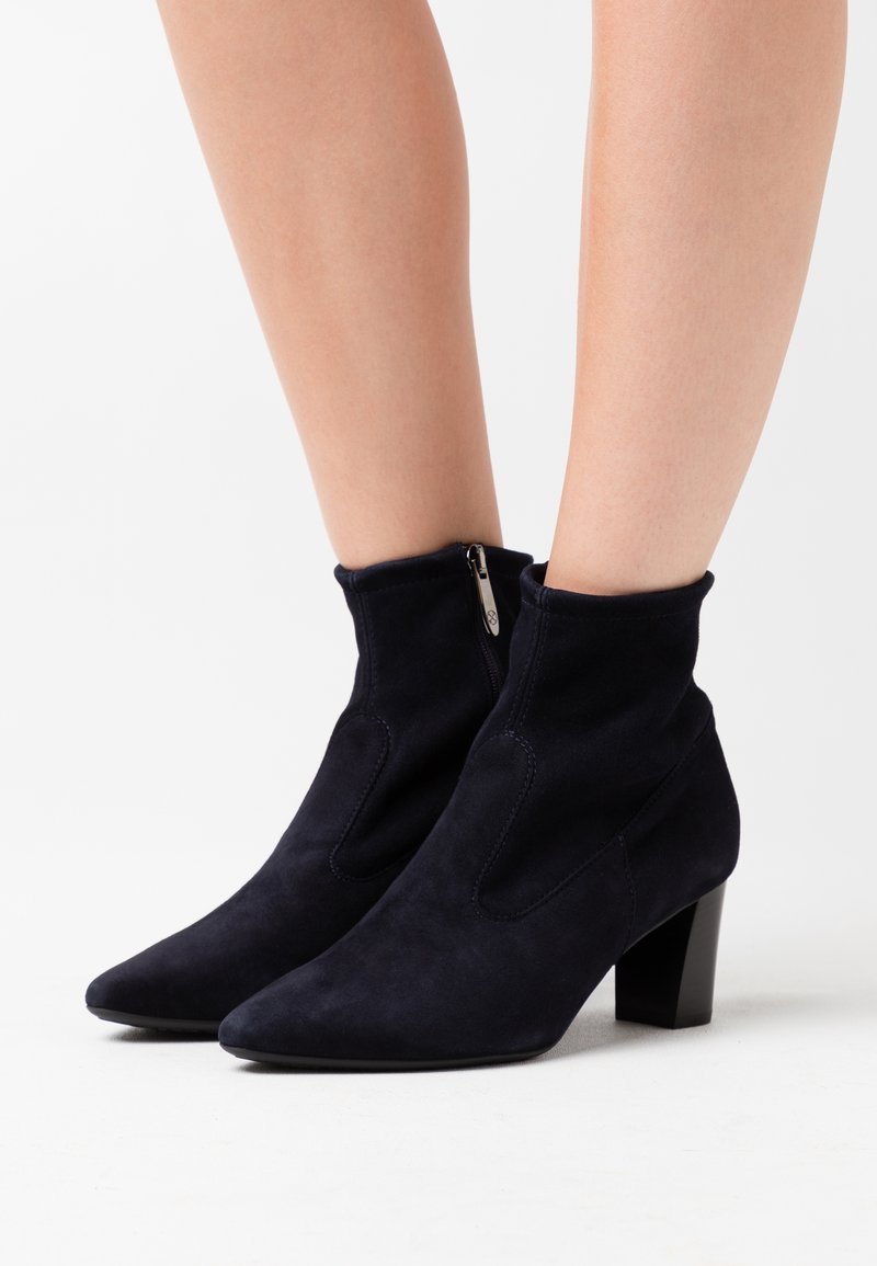 Botas de ante azul marino hasta el tobillo con punta afilada, que presentan un cierre de cremallera y un robusto tacón cuadrado. Textura suave y diseño ajustado.