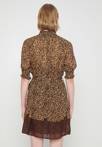 Vestido con estampado de leopardo marrón, mangas abullonadas, cuello fruncido y cintura elástica. Bajo semitransparente con un panel más oscuro. Con un patrón en toda su superficie.