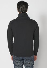 Fekete pulóver magas gallérral, texturált ujjakra és sima testre. Fitted dizájnnal és bordás mandzsettákkal rendelkezik, hogy kényelmesen illeszkedjen.