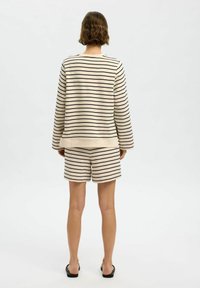 Pruhovaný, lehký krémový svetr s černými pruhy, spárovaný s odpovídajícími šortkami. Volný střih, dlouhé rukávy, lem končí u poloviny stehen.