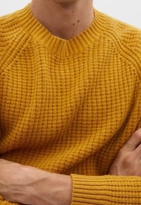 Mustard yellow textured sweater with a ribbed neckline and cuffs, featuring a chunky knit pattern and raglan sleeves.