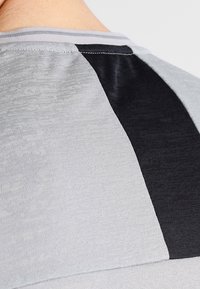 Camiseta deportiva gris y negra con un patrón texturizado, un bloqueo de color distintivo y un escote reforzado.