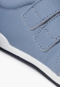 Scarpa sintetica azzurro chiaro con cinturini in Velcro, finitura texturizzata e suola in gomma bianca con bordo nero. Dettaglio di cuciture ben visibili sui cinturini.