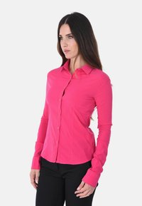 Camicia aderente a maniche lunghe di un vivace rosa, con colletto classico e chiusura a bottoni, dotata di polsini piatti e una superficie liscia.