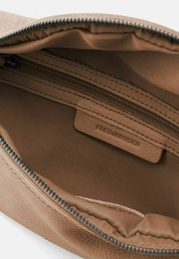 El interior de la bolsa de cuero marrón presenta una forma suave y estructurada, un bolsillo con cremallera y una etiqueta de marca sutil, con un forro de tela suave.