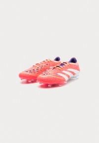 Botas de fútbol de un vibrante color naranja con rayas blancas, que presentan un upper texturizado y un talón de soporte. Las botas tienen un diseño elegante y aerodinámico.