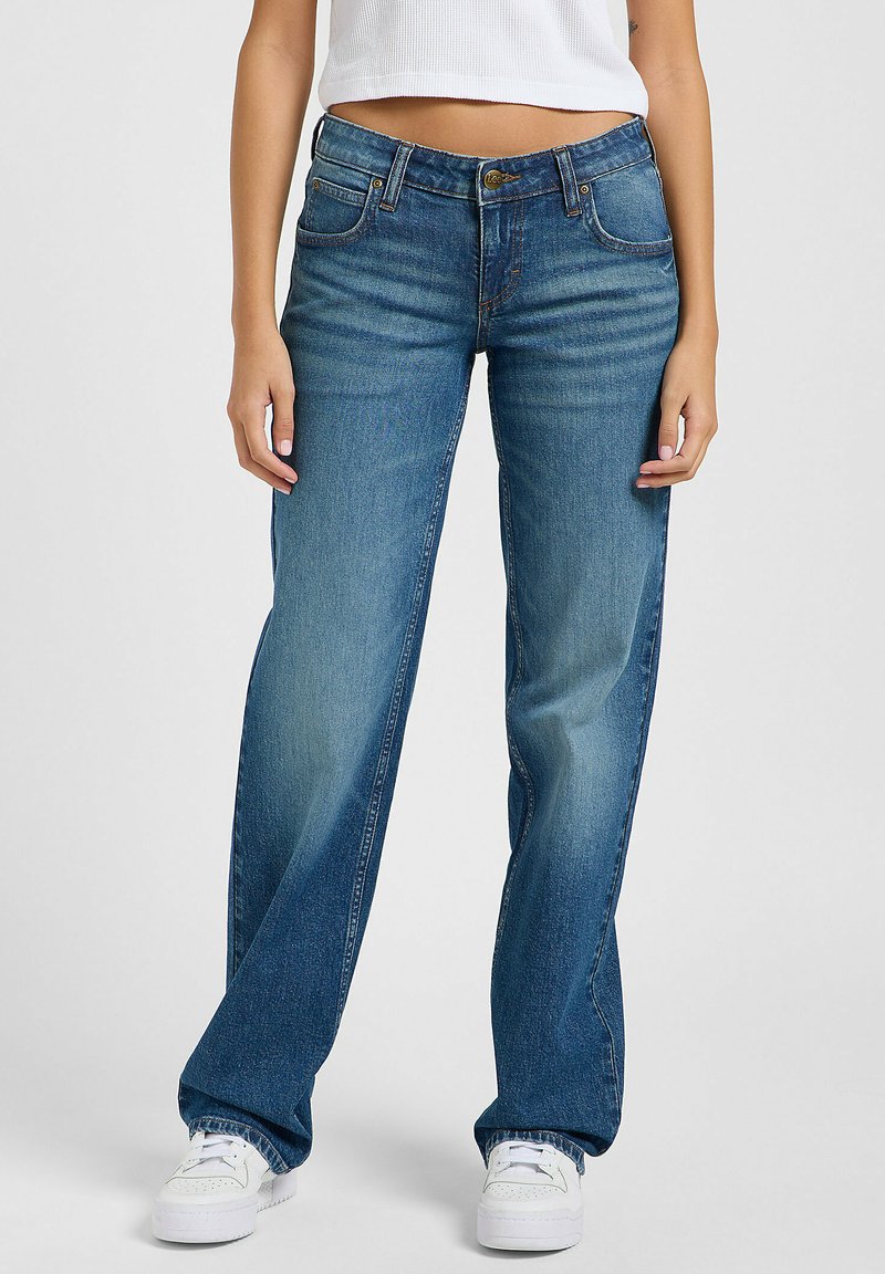 Jeans de mezclilla azul con un corte relajado, que cuentan con cinco bolsillos, un cierre de botones y un suave desgaste. Combinados con zapatillas blancas.