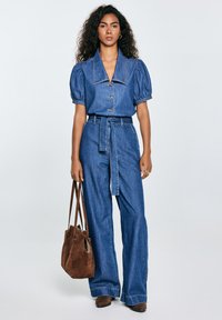 Denim-overallit puff-hihoilla, suurella kauluksella ja etupainikkeilla. Yhdistetty ruskean samettisen laukkuun ja vastaaviin nilkkasaappaisiin.