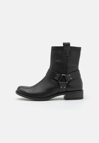 Botas de cuero negro hasta el tobillo con punta redonda y tacón bajo. Incluyen una correa con hebilla y remaches, destacando el diseño industrial.