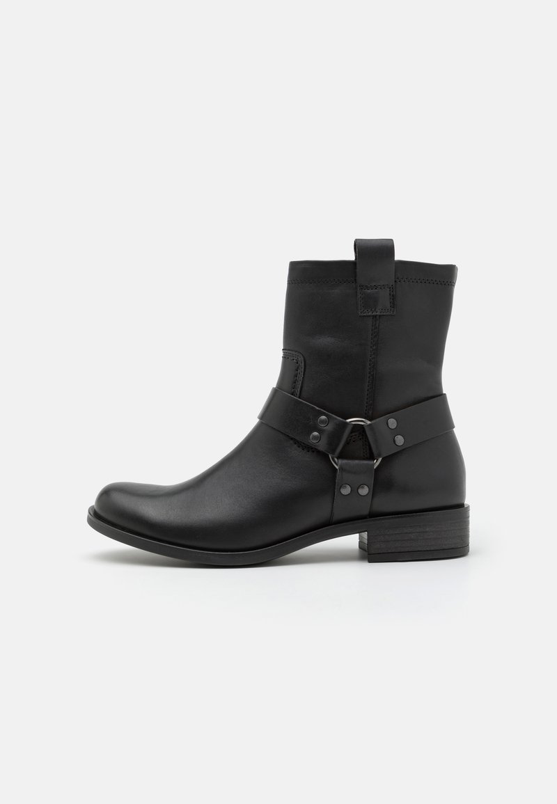 Botas de cuero negro hasta el tobillo con punta redonda y tacón bajo. Incluyen una correa con hebilla y remaches, destacando el diseño industrial.