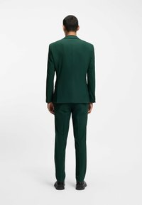 Dunkelgrüner maßgeschneiderter Anzug mit einer taillierten Jacke und Hose. Glatter Stoff, schlanke Form und minimalistisches Design mit dezentem Nähen.