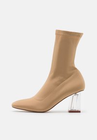 Alaston sukka-tyylinen nilkkasaapas, sileä kangas, terävä kärki, läpinäkyvä block-korko, joustava yläosa, vähäiset ompelut.