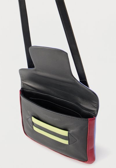 Μαύρο δερμάτινο τσαντάκι χιαστί με κόκκινες πλαϊνές πάνελ, λωρίδες σε λάιμ πράσινο οριζόντια στην μπροστινή τσέπη, και ανοιχτό πάνω καπάκι που δείχνει το εσωτερικό.