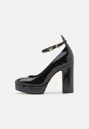 Scarpe con tacco alto in vernice nera, con piattaforma, cinturino alla caviglia e dettagli in metallo dorato. Punta arrotondata e superficie lucida.