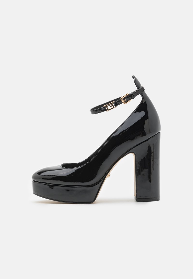 Scarpe con tacco alto in vernice nera, con piattaforma, cinturino alla caviglia e dettagli in metallo dorato. Punta arrotondata e superficie lucida.