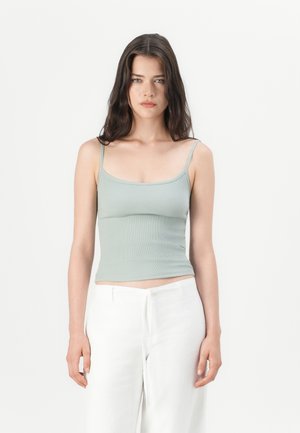 Lys grønn ribbet tanktopp med tynne stropper. Har en tettsittende design og en rett utringning. Kombinert med hvite, løstsittende bukser.