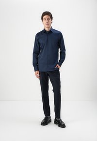 Cămașă navy cu nasturi, cu mâneci lungi, asortată cu pantaloni întunecați și pantofi negri. Țesătură netedă, croi ajustat și design structurat.