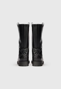Juodos mid-calf ilgio batai su storais padais ir dekoratyvine pynimo odos detale gale, pateikti ant vientiso balto fono.