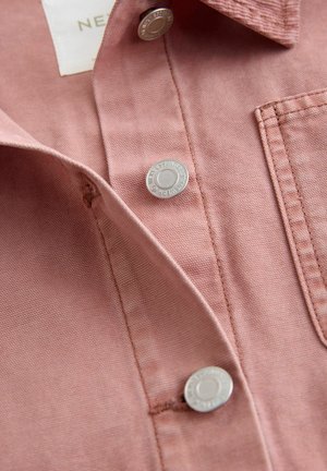 Roseskåret skjorte med et tekstureret stof, der har sølvfarvede trykknapper og en brystlomme. Kraven er foldet, hvilket viser syningsdetaljer.