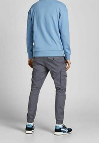 Ljusblå sweatshirt med ribbade ärmmuddar, ihopparad med grå cargobyxor som har sidofickor och svarta sportskor med blå detaljer.