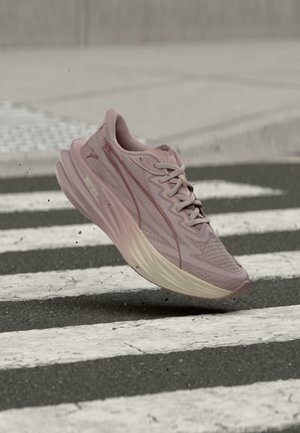 Chaussure de course violet clair en l'air au-dessus d'un passage piéton sur une route asphaltée.